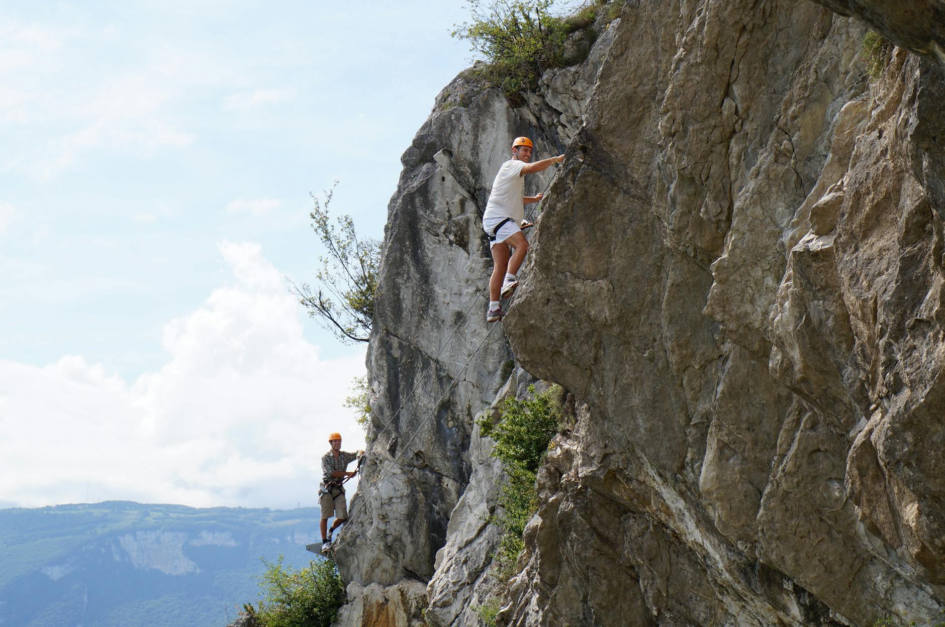 Two climbers ascend a rugged cliff, showcasing adventure and skill.